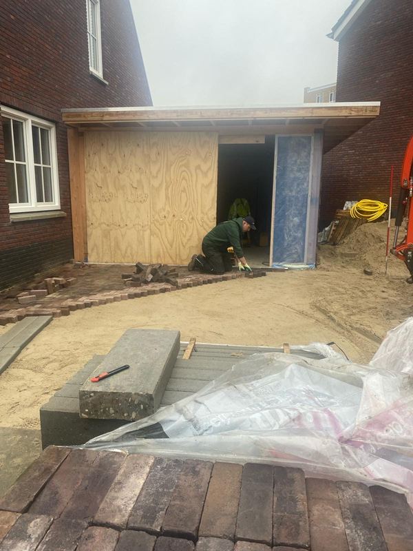 Bestratingswerk met gebakken klinkers onder een nieuwe houten overkapping bij een woning in aanbouw